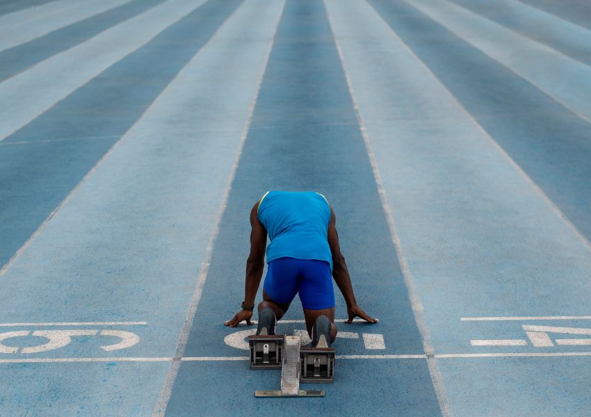 Como manter o foco e atingir seus objetivos: um atleta na pista de corrida, abaixado pronto para iniciar a corrida.